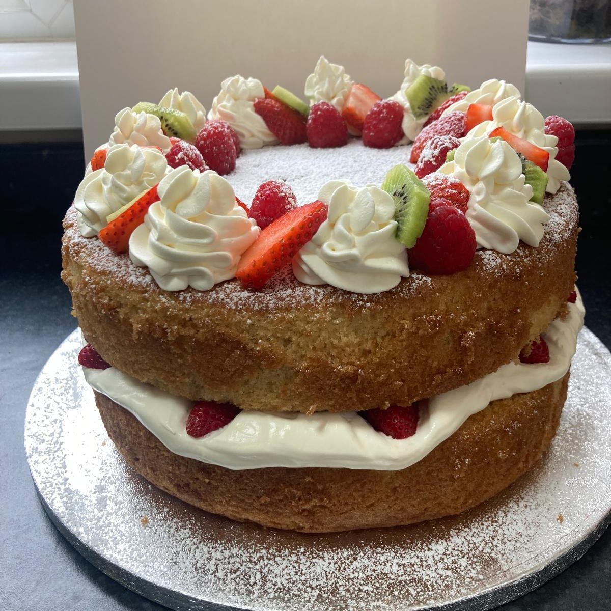 A Victoria sponge filled with cream, topped with piped cream, strawberries, raspberries and kiwi, baked by the Kongwa family in Medway